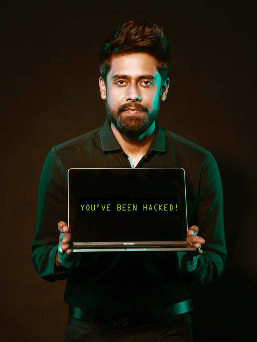 Ein stehender Mann schaut ungebegeistert und zeigt den Bildschirm eines Laptops auf dem angezeigt wird: You've been hacked!