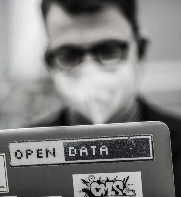 Portrait von Josef Hörmandinger in Schwarz.-Weiß mit Maske und Laptop mit einem Sticker auf dem Open Data sthet.